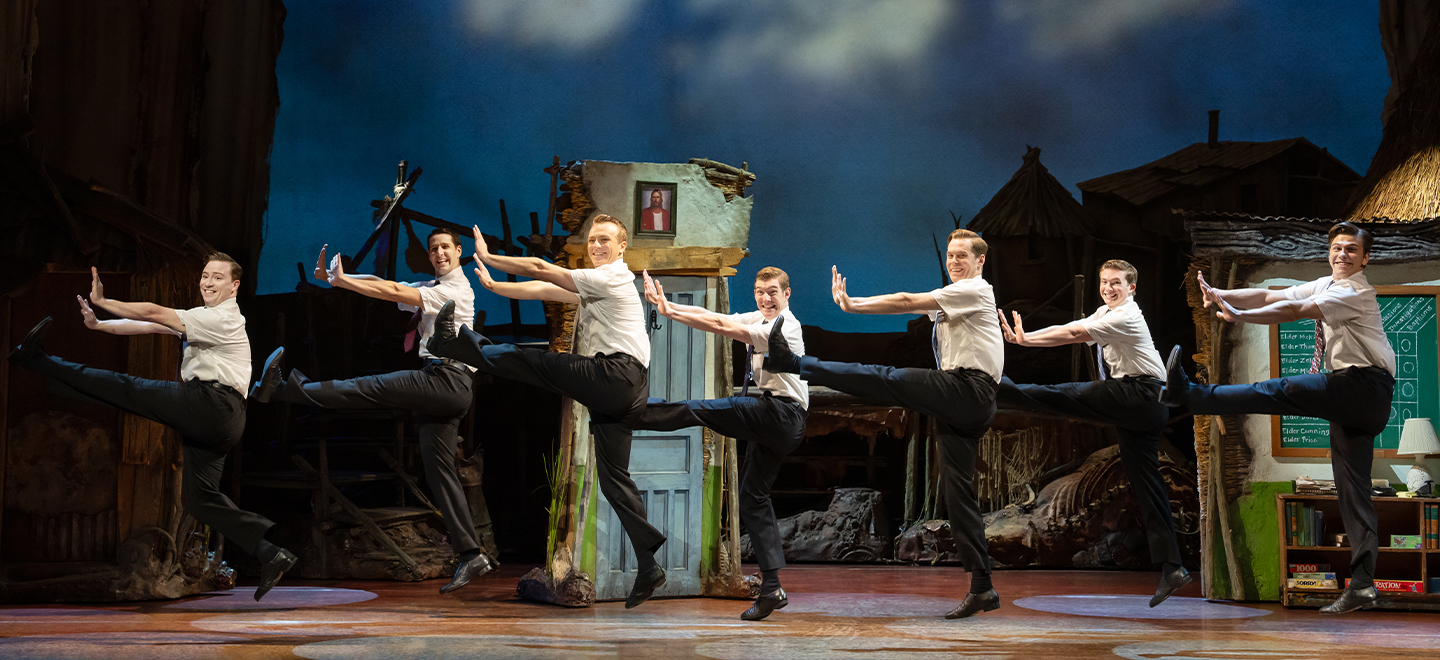 The Book of Mormon cast performing a kick line onstage.