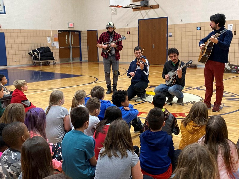 Musicians performing on guitars, banjos, and violin for a class of students