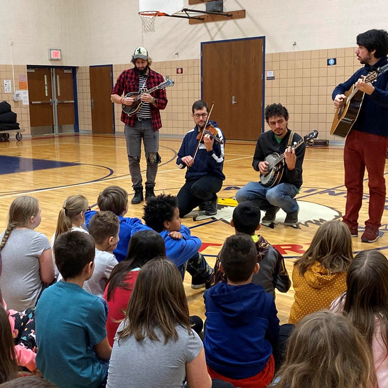 Musicians performing on guitars, banjos, and violin for a class of students