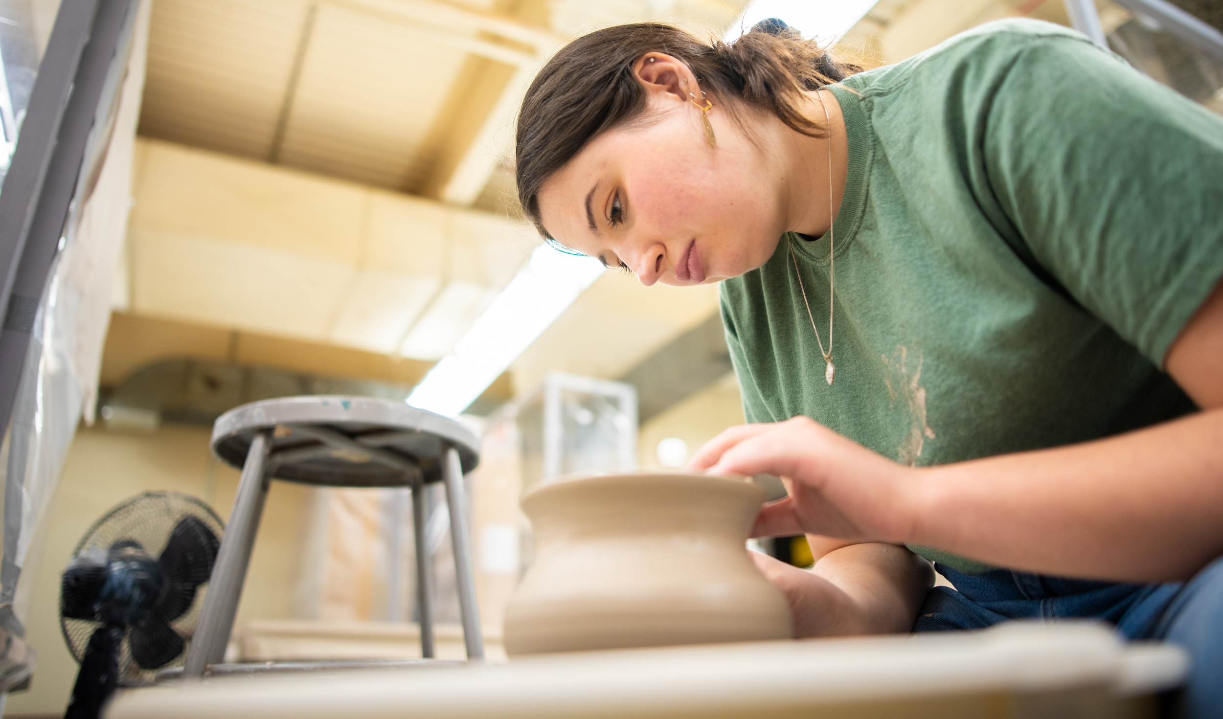 A woman working intently on a clay pot on a pottery wheel