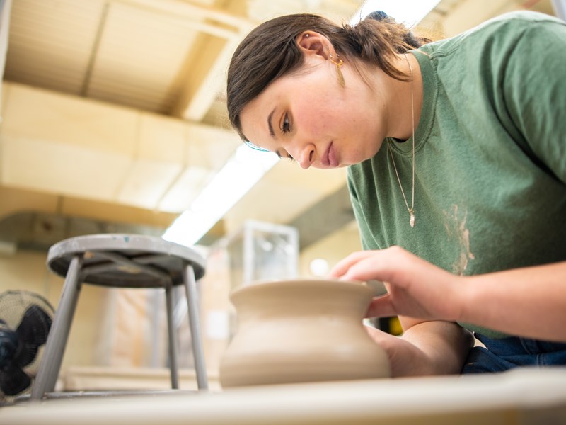 A woman working intently on a clay pot on a pottery wheel