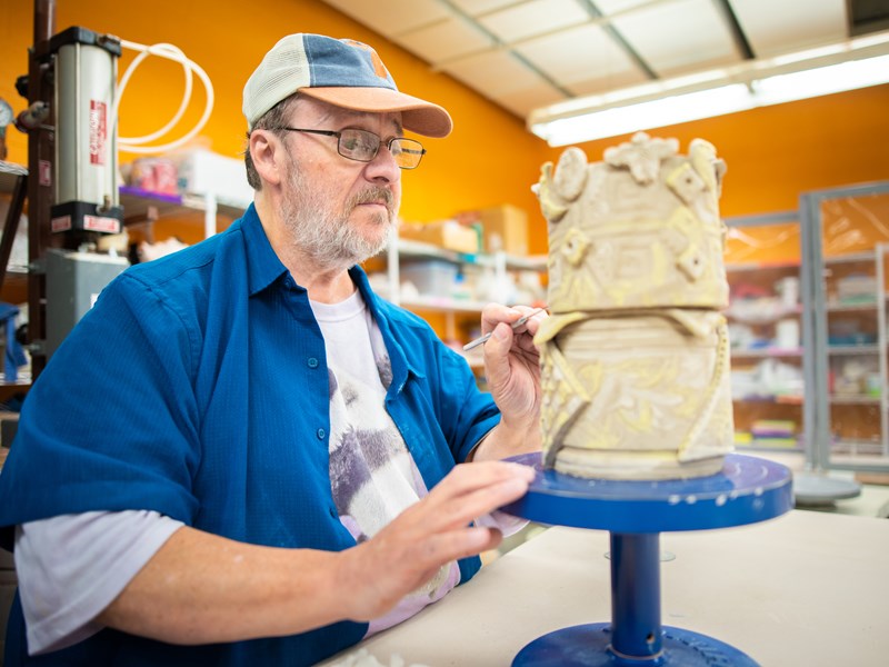 A man doing finishing touches with a fine brush on an intricate ceramic